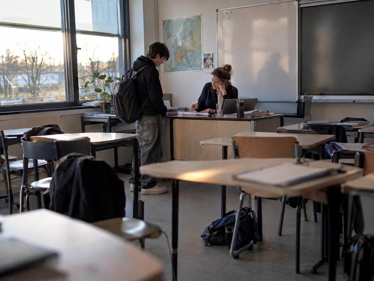 Leeg lokaal na de les: één leerling staat nog bij het bureau van de docent, die met hem meekijkt